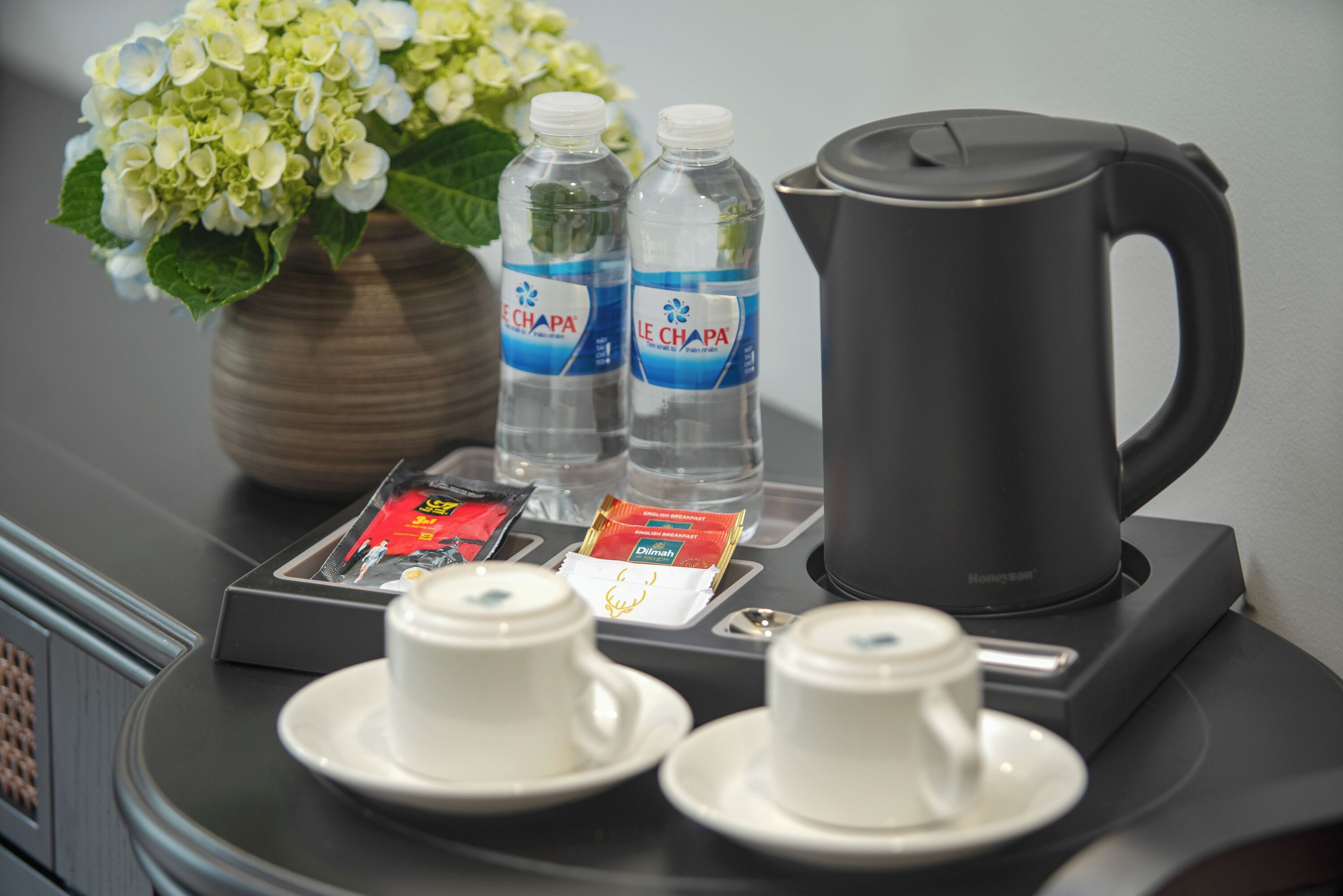 A table with two cups, two bottles of water, a coffee pot, and a packet of tea.