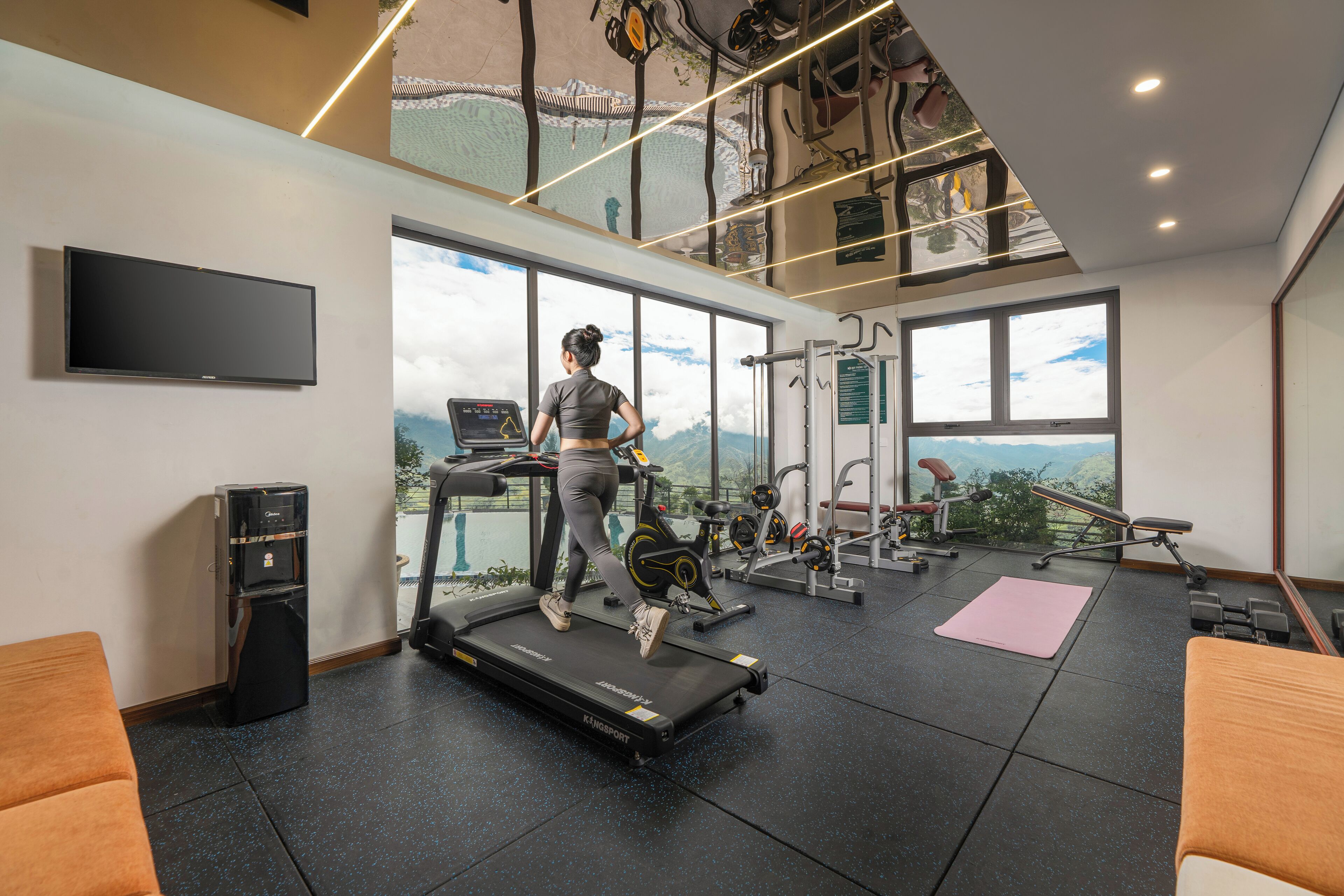 A gym with a treadmill, exercise bikes, and weights. There is a large window with a view of mountains.