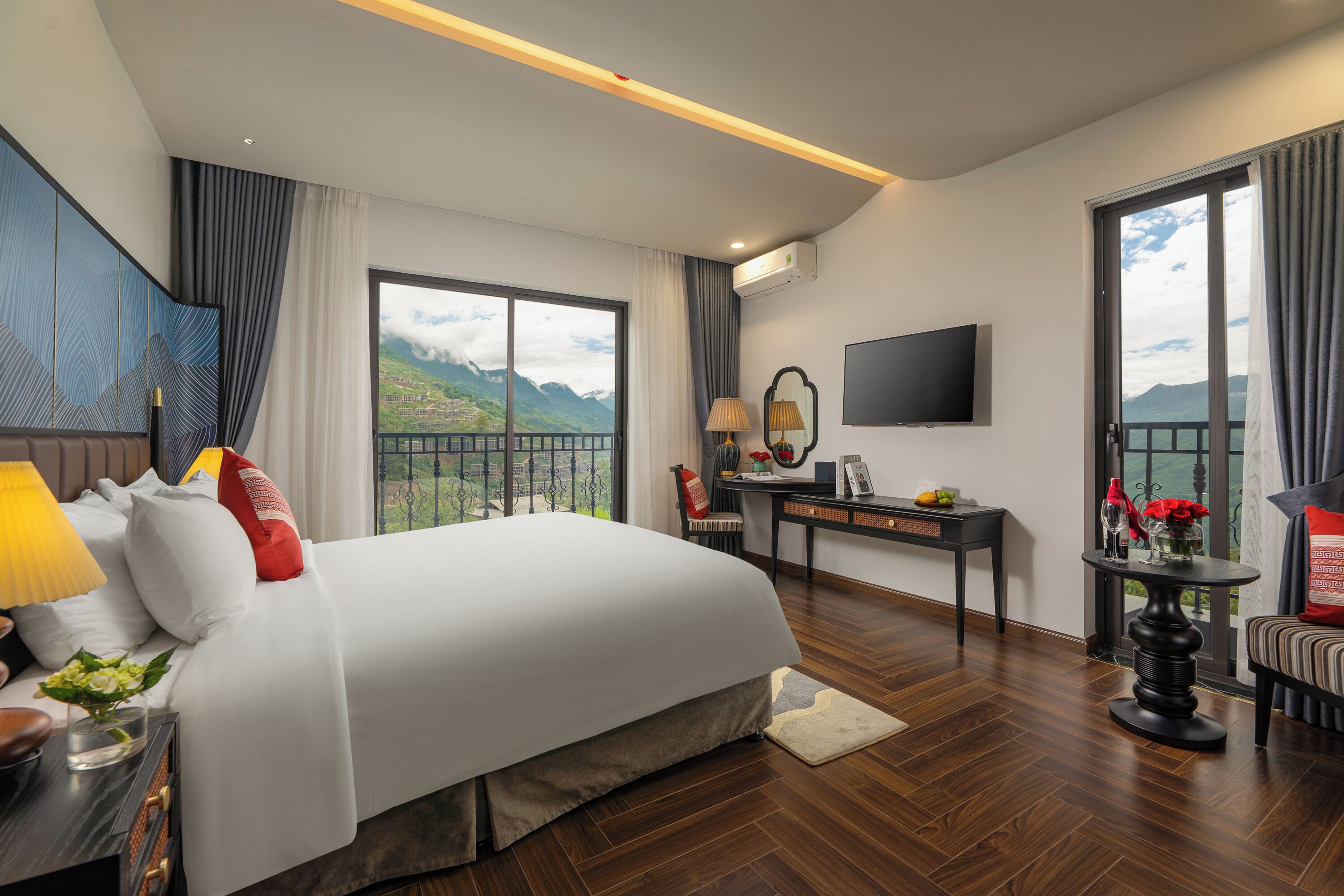 Habitación de hotel con una cama grande, un escritorio, un televisor y un balcón con vista a la montaña.