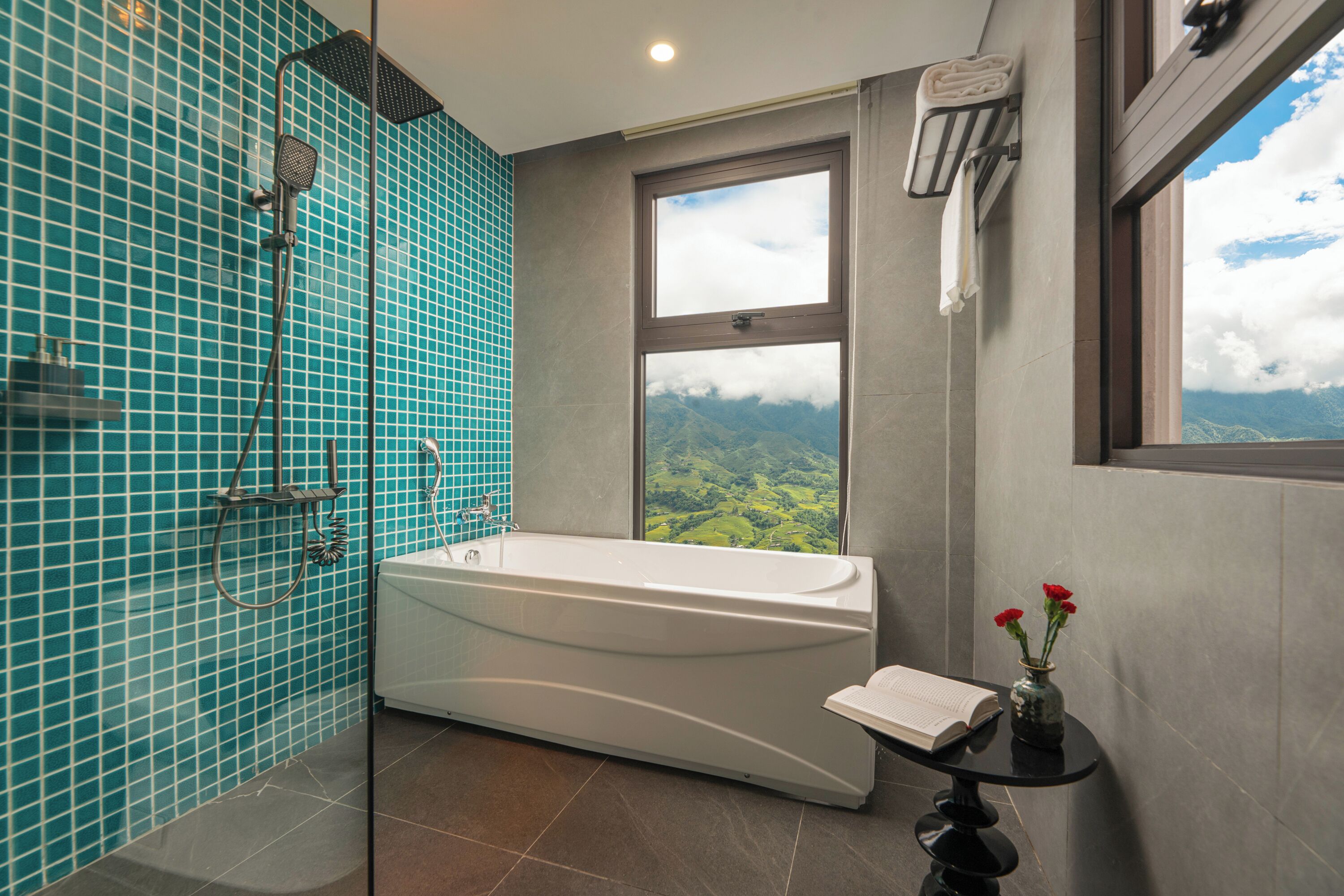 A bathroom with a bathtub, a shower, and a window with a mountain view.