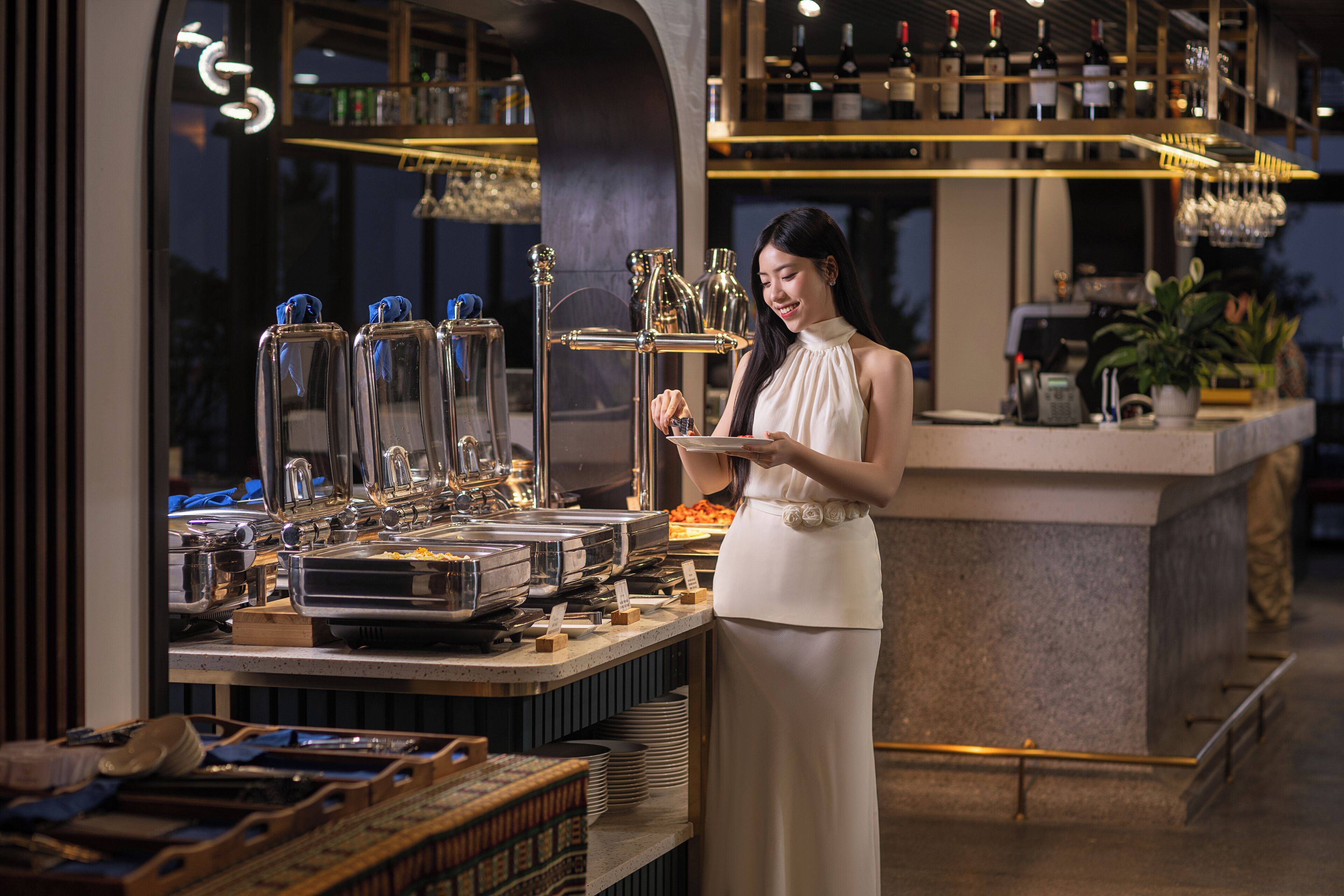 A bar area with a woman serving drinks, a wine rack, and a buffet with various dishes.