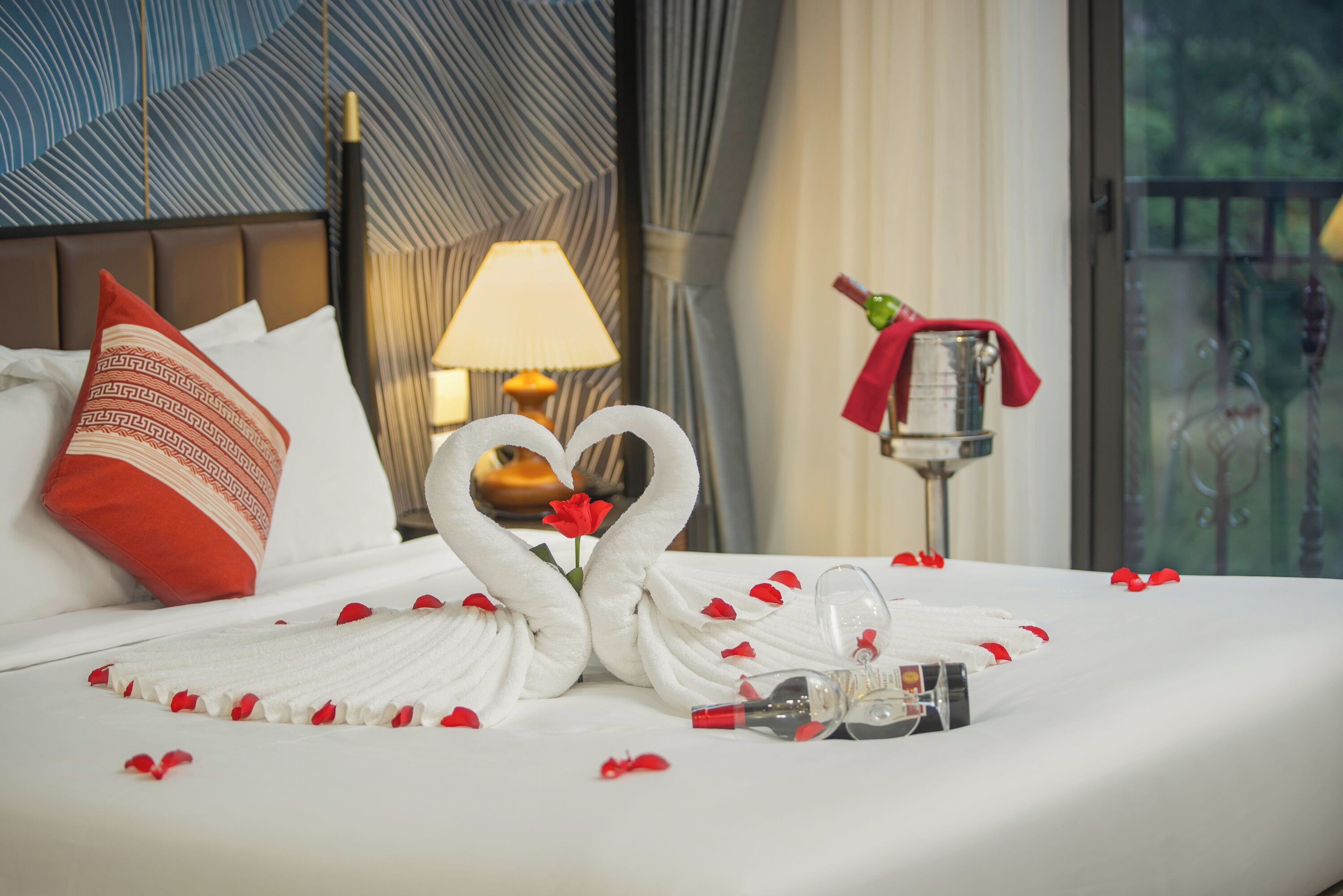 A hotel room with a bed, a lamp, a bottle, and a decorative item on the nightstand.