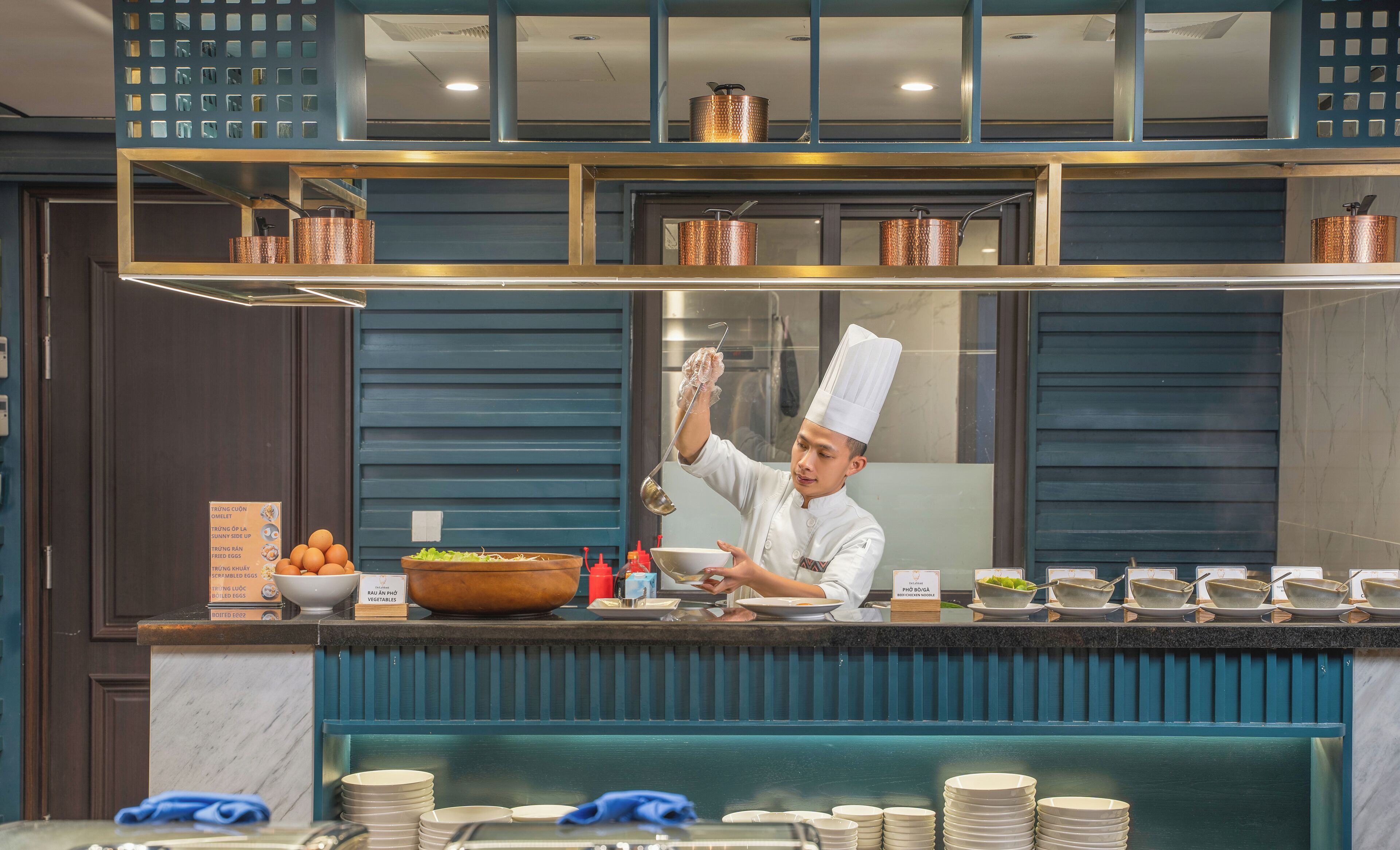 A chef preparing food behind a counter with various dishes and ingredients visible.