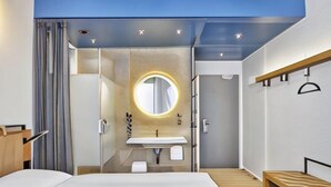 A modern hotel room with a bed, a round mirror, a sink, and a shower. - Sunday Düsseldorf Seestern (Dusseldorf)