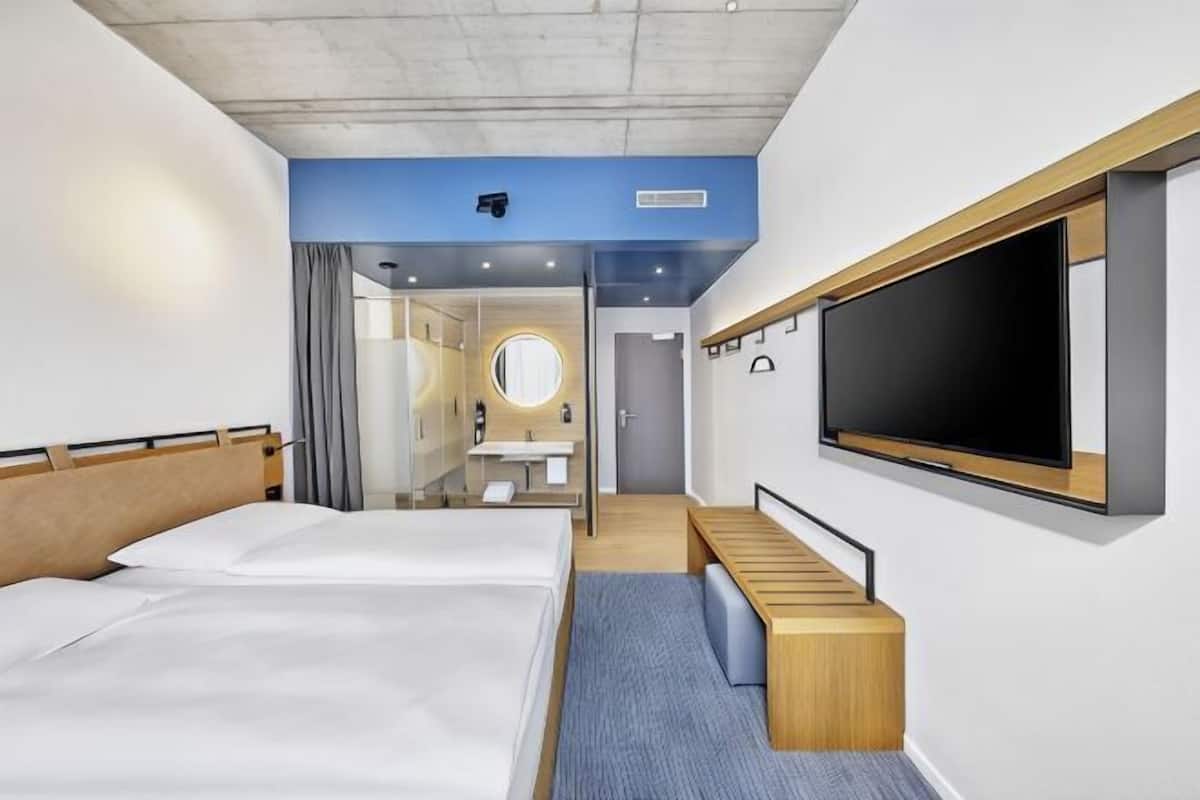 Ett hotellrum med två sängar, en TV, ett badrum med spegel och ett skrivbord.