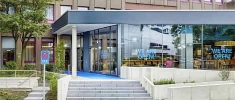 A modern hotel entrance with a glass facade, a covered staircase, and a 'We are open' sign.