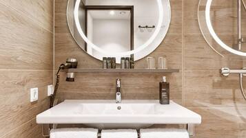 Un baño con un lavabo blanco, un espejo redondo y un perchero con toallas.