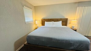 A neatly made bed with a wooden headboard, two bedside lamps, and a window with blinds.