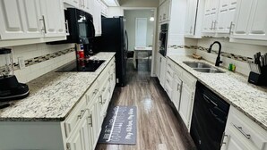 A modern kitchen with white cabinets, granite countertops, a black refrigerator, and a dishwasher.