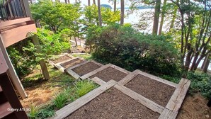 Een tuin met verhoogde borders, een houten terras en uitzicht op een waterpartij.