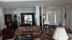 Een woonkamer met een bloemenbank, een rode fauteuil, een salontafel en een kroonluchter.