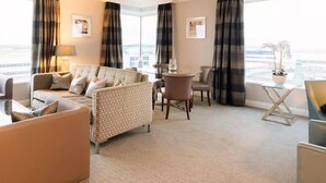 A hotel room with a sofa, armchairs, a small table, and a view of the city. - Sofitel London Gatwick (Horley)