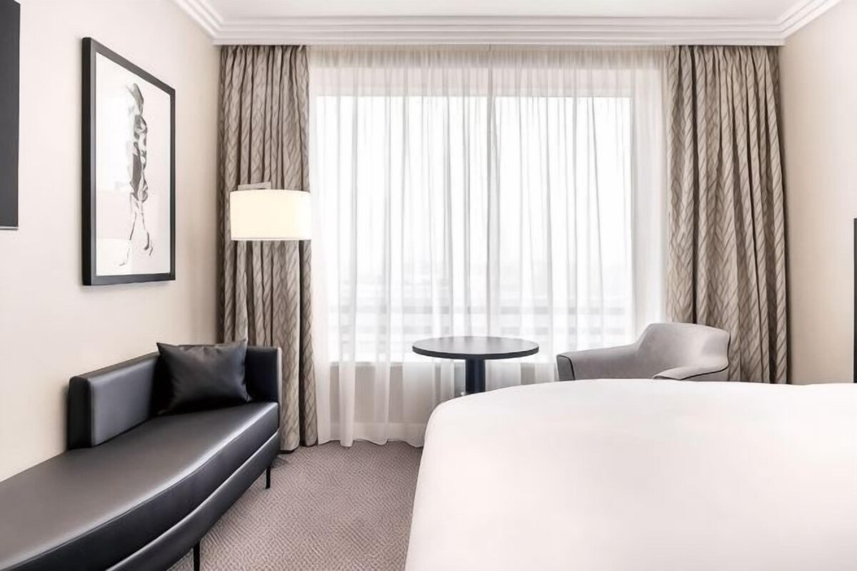 A hotel room with a bed, a sofa, a chair, a small table, and a window with curtains.