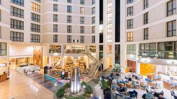 A multi-level hotel atrium with a central staircase, retail shops, and seating areas.