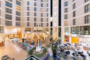 A multi-level hotel atrium with a central staircase, retail shops, and seating areas. - Sofitel London Gatwick (Horley)