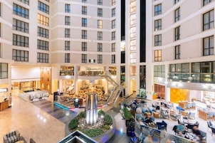 A multi-level hotel atrium with a central staircase, retail shops, and seating areas.