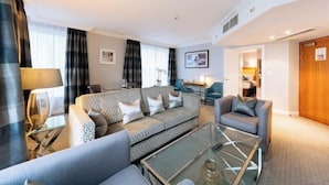A modern living room with a sofa, armchairs, a glass coffee table, and a dining area with a table and chairs. - Sofitel London Gatwick (Horley)