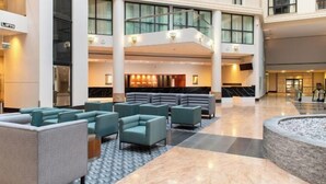 A spacious lobby with multiple seating areas, a central staircase, and a reception desk. - Sofitel London Gatwick (Horley)