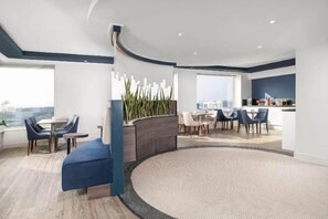 A modern hotel lobby with a curved seating area, a central plant, and a view of the city. - Sofitel London Gatwick (Horley)
