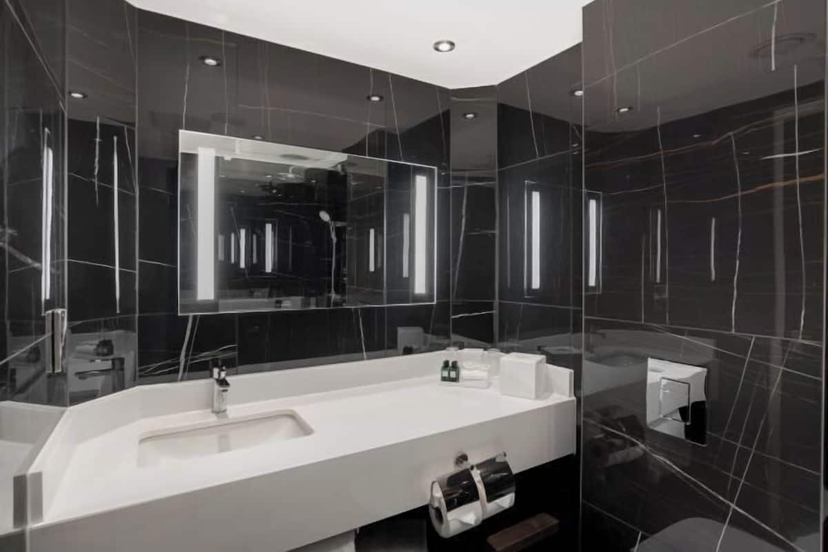 A modern bathroom with a large mirror, a white sink, and dark marble walls.