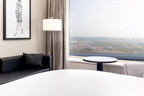 A hotel room with a large window offering a view of an airport. - Sofitel London Gatwick (Horley)