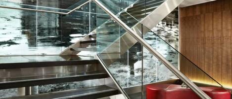 Una escalera moderna con barandas de cristal y un muro de madera.