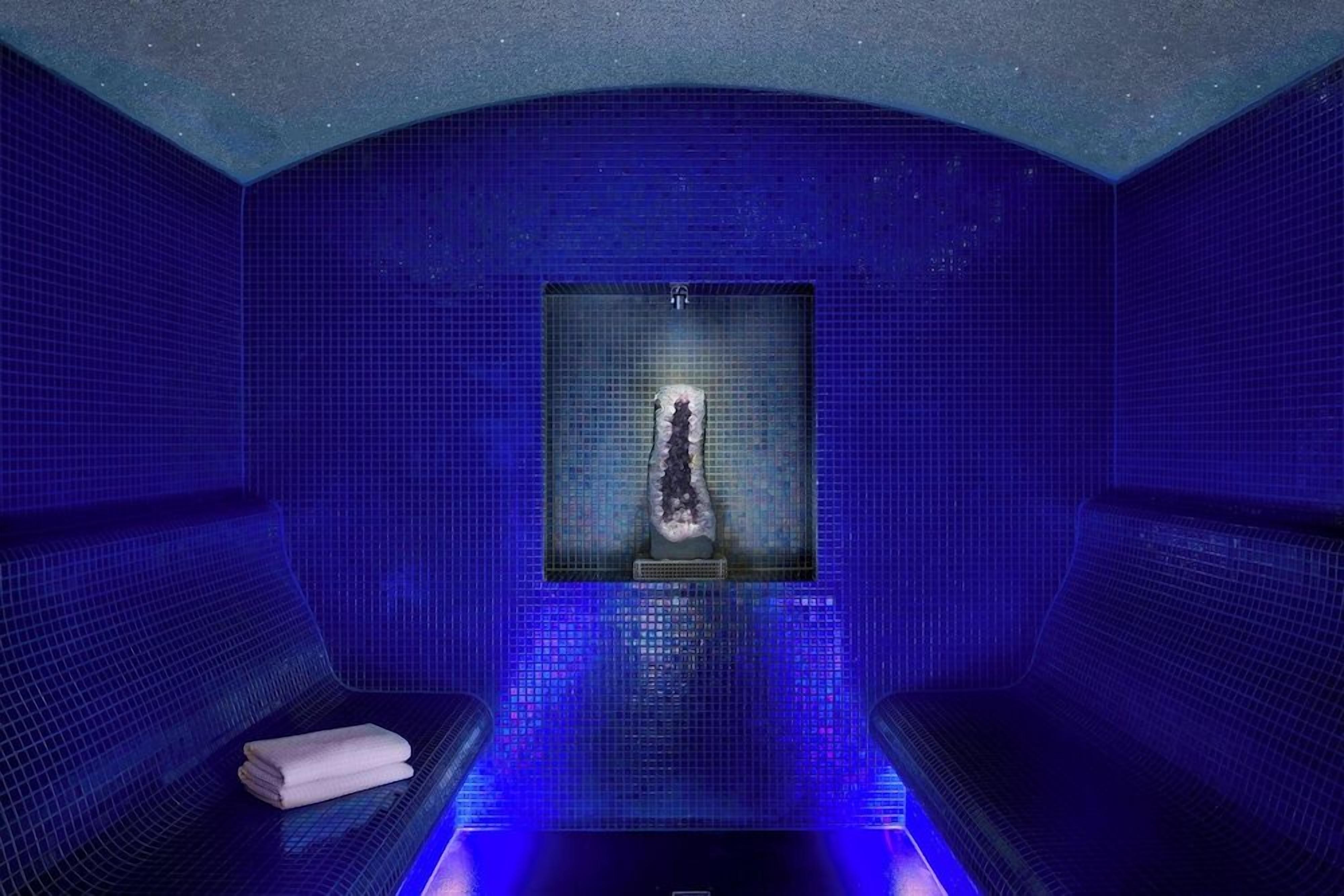 Una habitación azulada con paredes de azulejos, un elemento central de agua y dos zonas de estar.