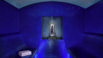Una habitación azulada con paredes de azulejos, un elemento central de agua y dos zonas de estar.