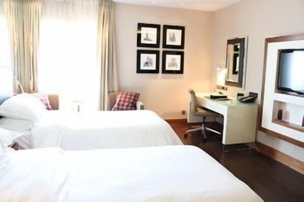 A hotel room with two beds, a desk, a chair, a TV, and framed pictures on the wall.