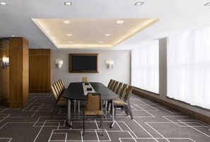 Un salón de conferencias con una larga mesa, sillas, un amplio ventanal y un diseño moderno en el techo.