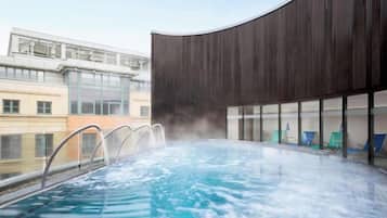 An indoor swimming pool with a curved edge, surrounded by a modern building with large windows and a wooden facade.