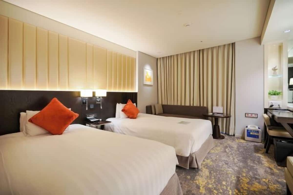 A hotel room with two beds, a desk, a chair, a small table, a mirror, and a bathroom.