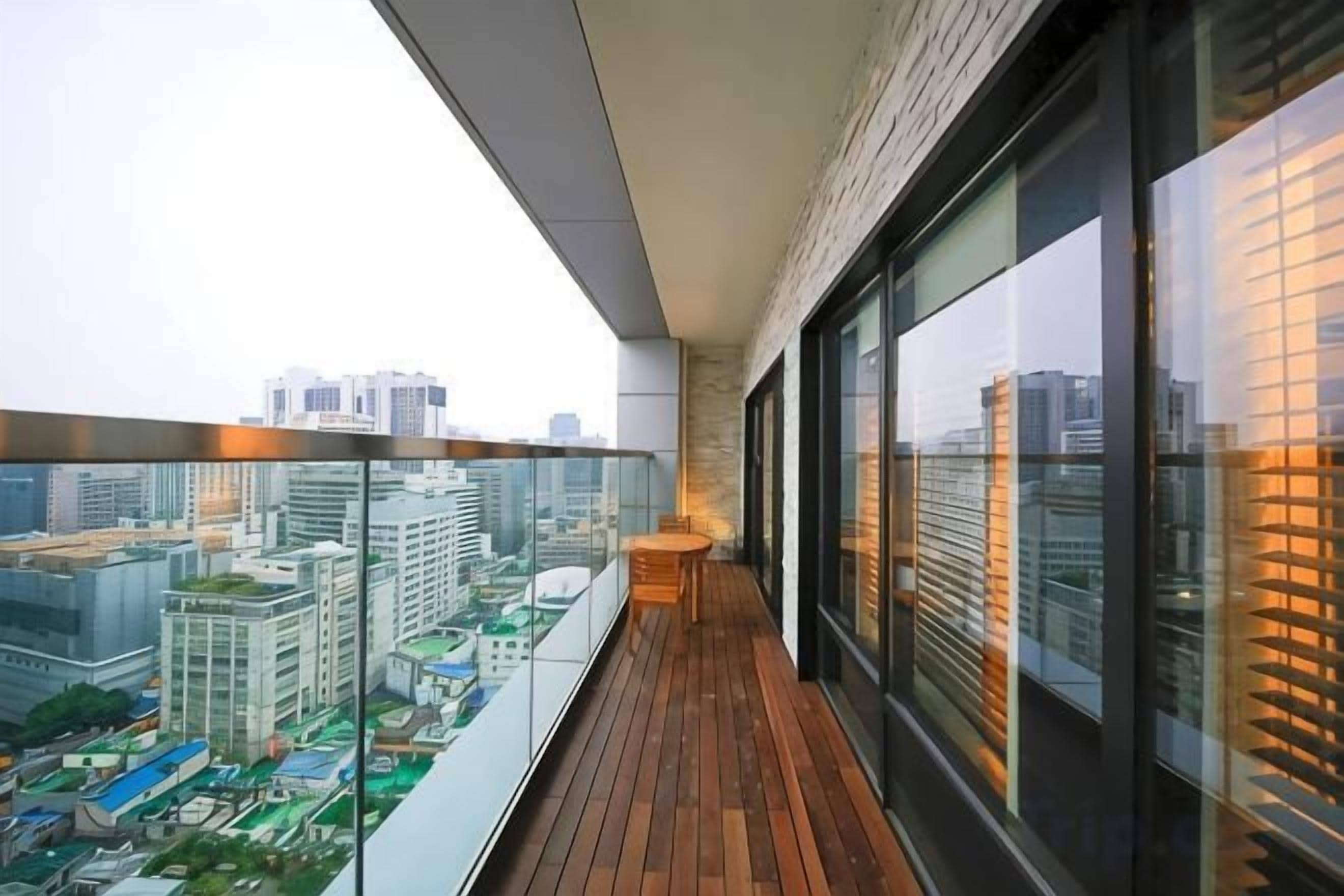 A balcony with a view of a cityscape, a wooden floor, and a glass railing.