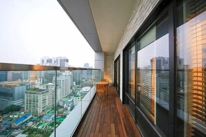 Un balcón con vistas a un paisaje urbano, piso de madera y barandilla de vidrio.