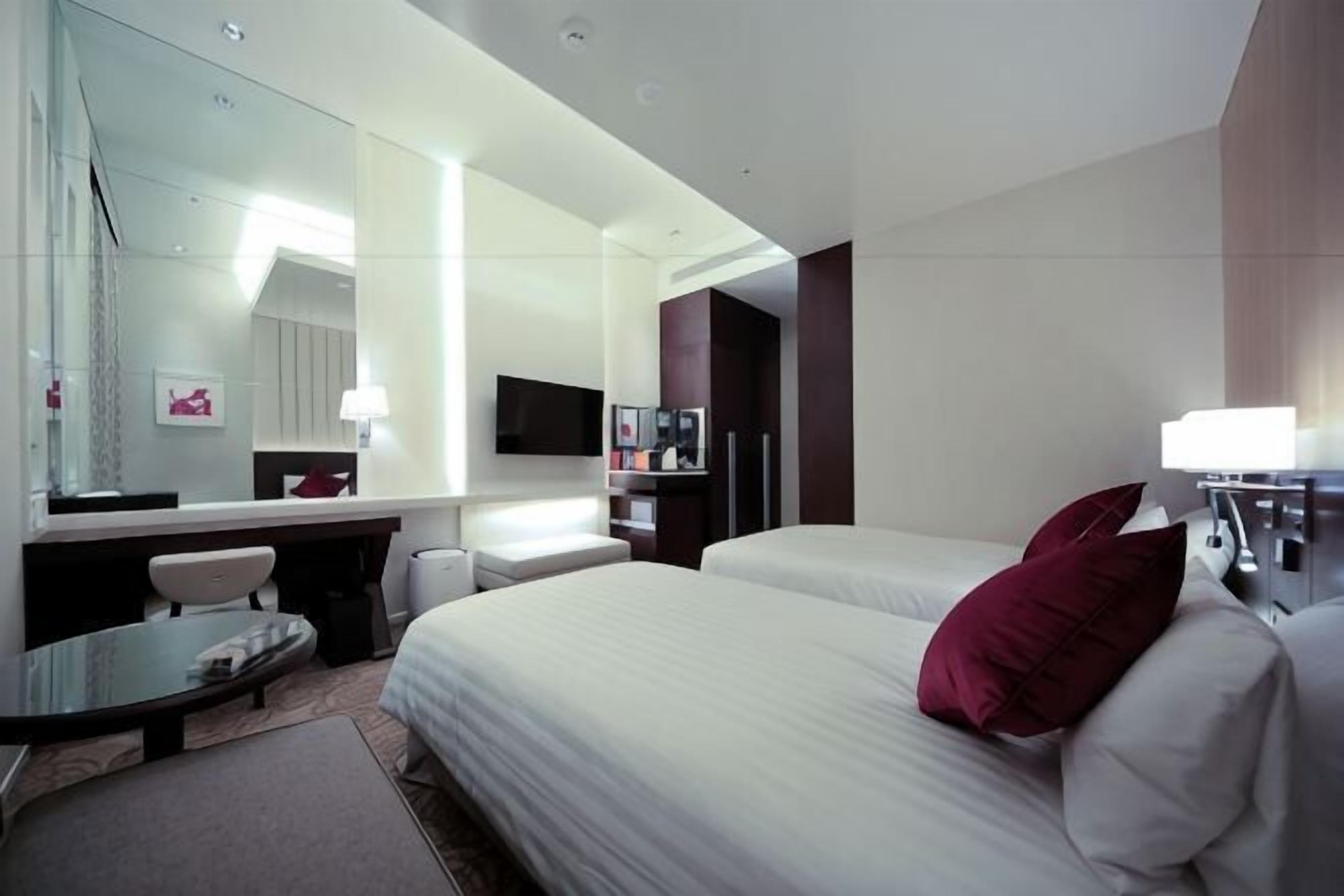Ein Hotelzimmer mit einem Bett, einem Schreibtisch, einem Sessel, einem Fernseher, einem Spiegel und einem Fenster.