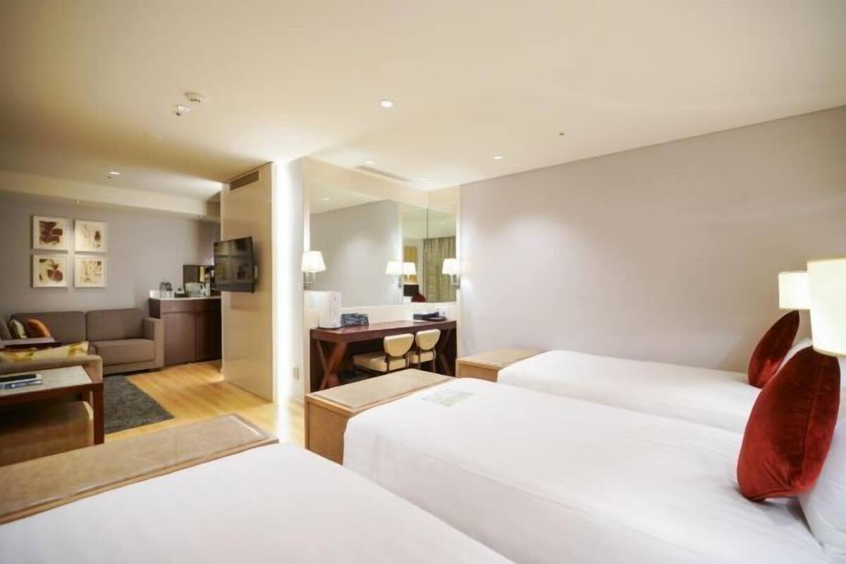 A hotel room with two beds, a desk, a chair, a sofa, and a dining table.