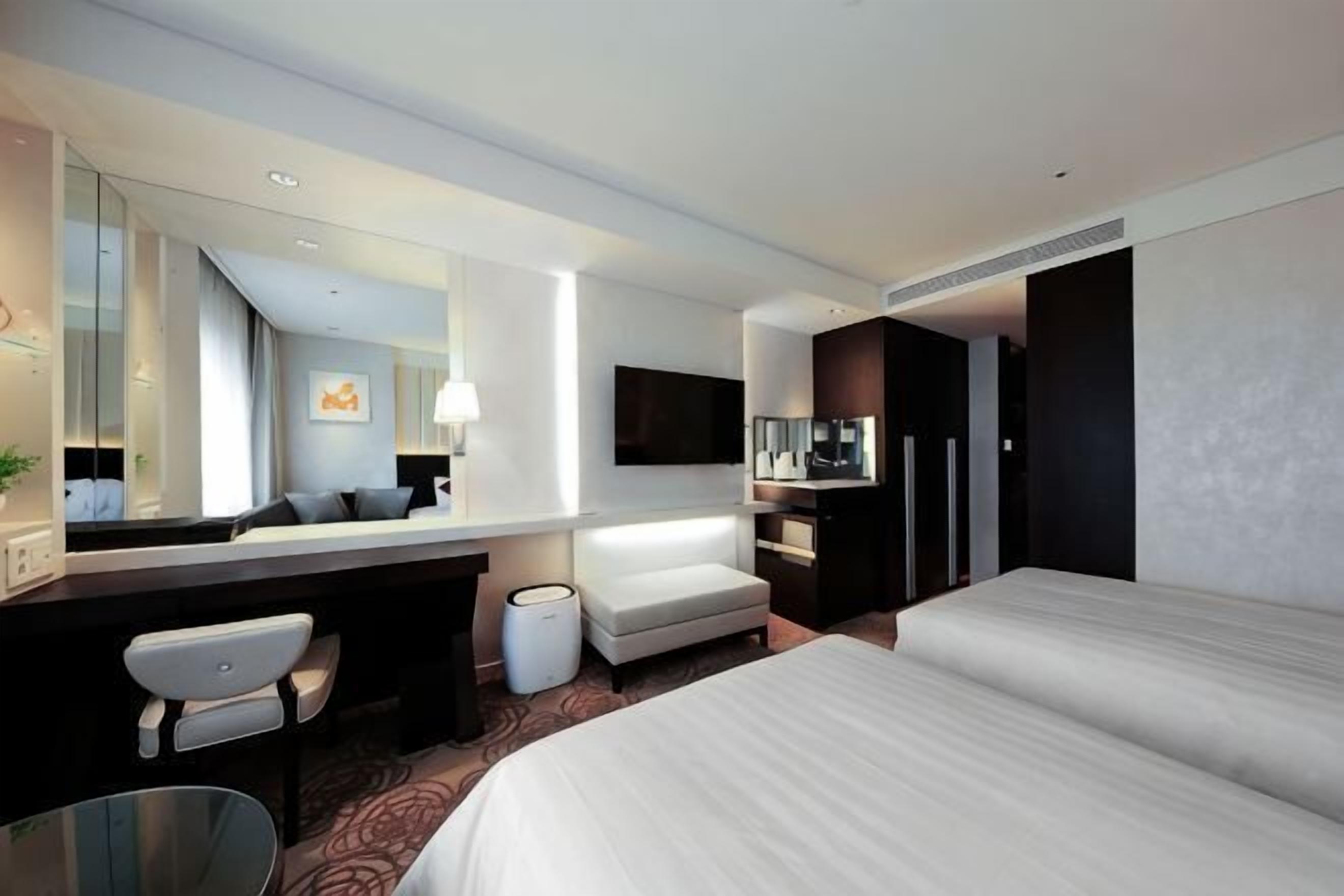 Ein Hotelzimmer mit Bett, Schreibtisch, Stuhl, Fernseher und einem großen Spiegel.