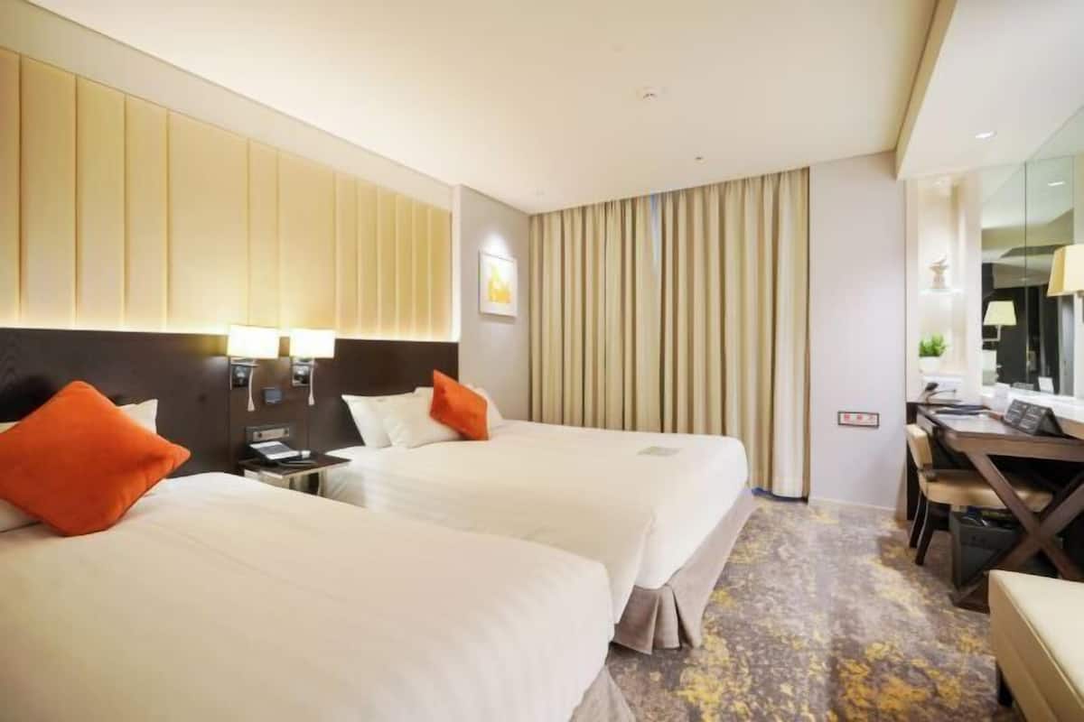 A hotel room with two beds, a desk, and a chair.