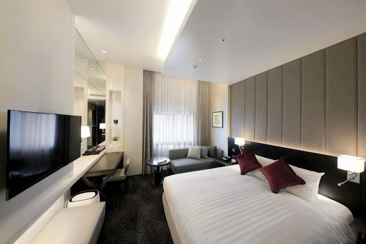 A hotel room with a large bed, a TV, a desk with a chair, a sofa, and a small table.