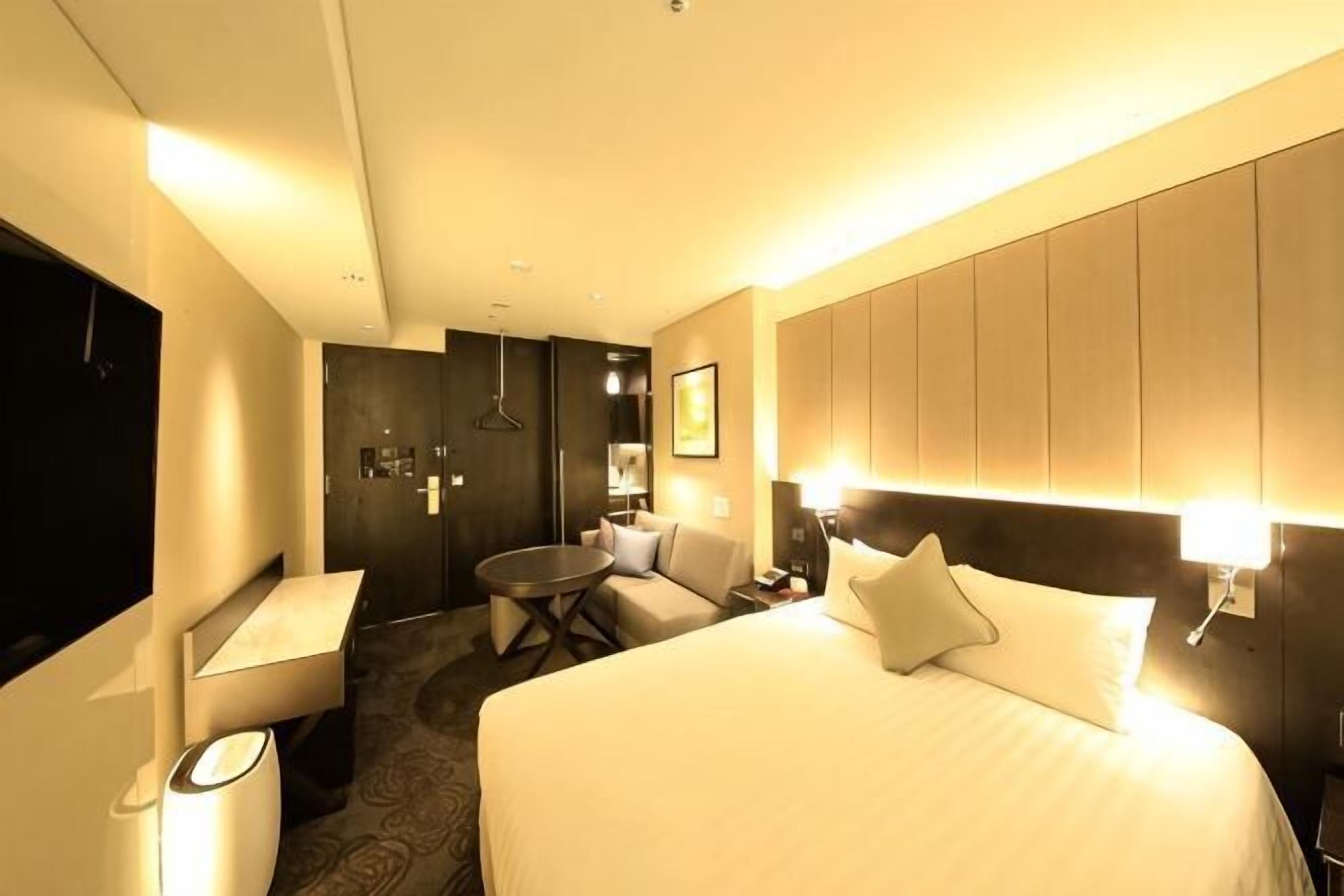 Ein Hotelzimmer mit Bett, Nachttisch, Stuhl, Schreibtisch und einem kleinen runden Tisch.