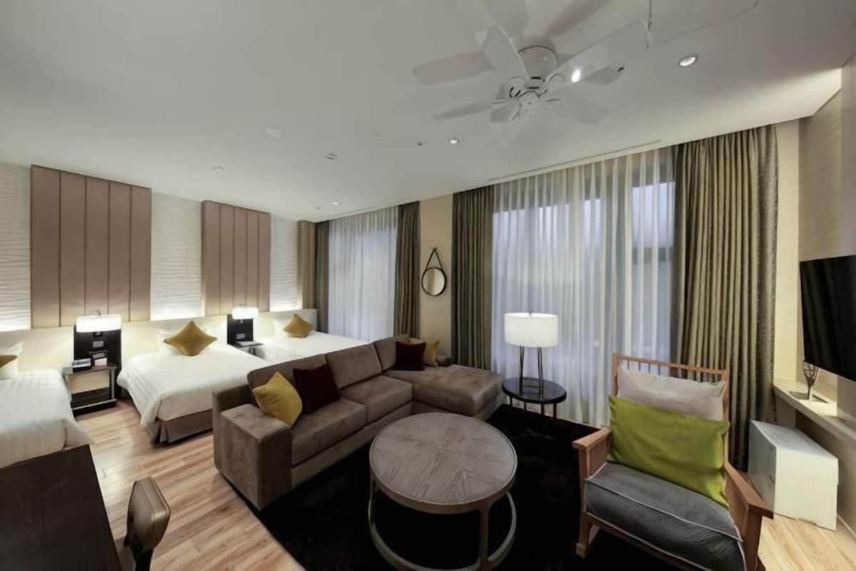 A hotel room with a bed, sofa, armchair, and round table.