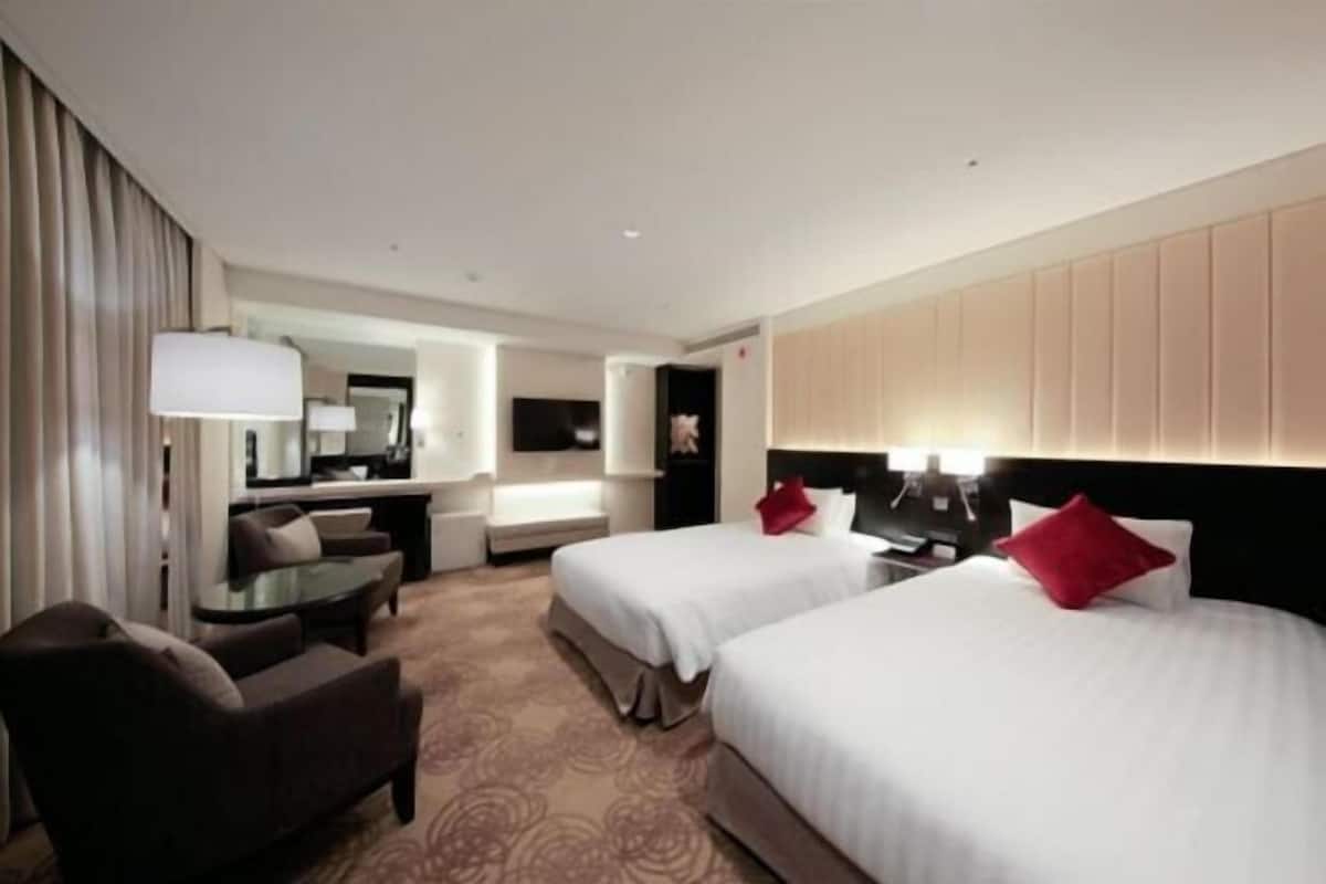 A hotel room with two beds, a sofa, a desk, and a mirror.