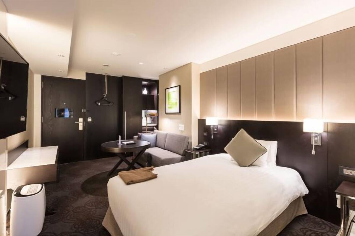 A hotel room with a large bed, a desk, a chair, a small table, and a sofa.