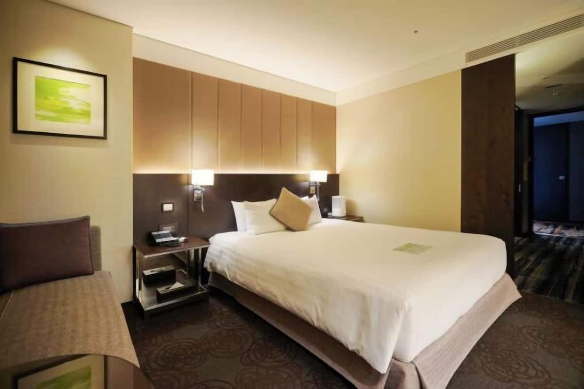 A hotel room with a bed, bedside tables, a desk, and a chair.