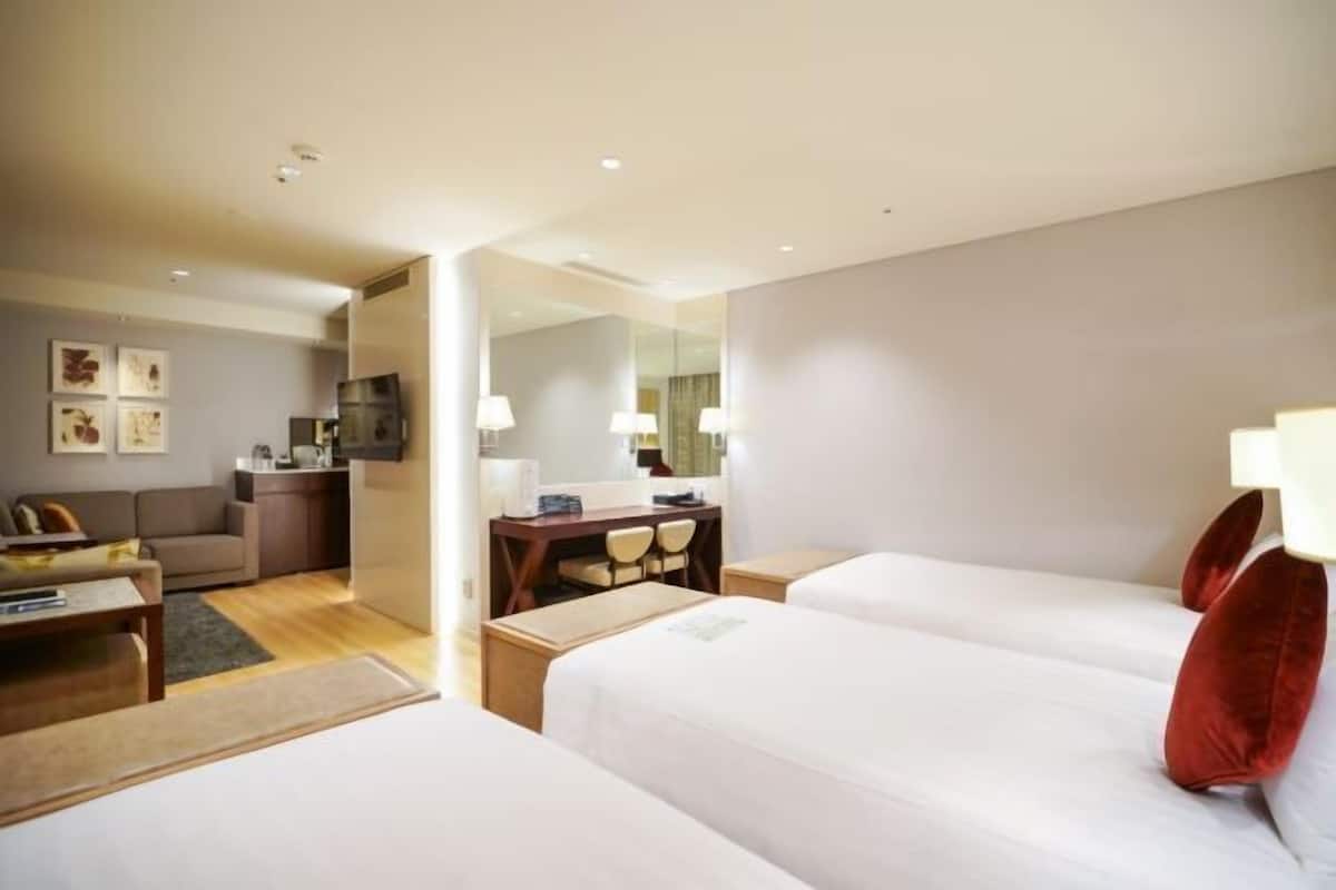 A hotel room with two beds, a desk, a chair, a sofa, a TV, and a dining area.