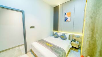 A modern hotel room with a neatly made bed, a bedside table with a phone, and a wall-mounted light fixture.