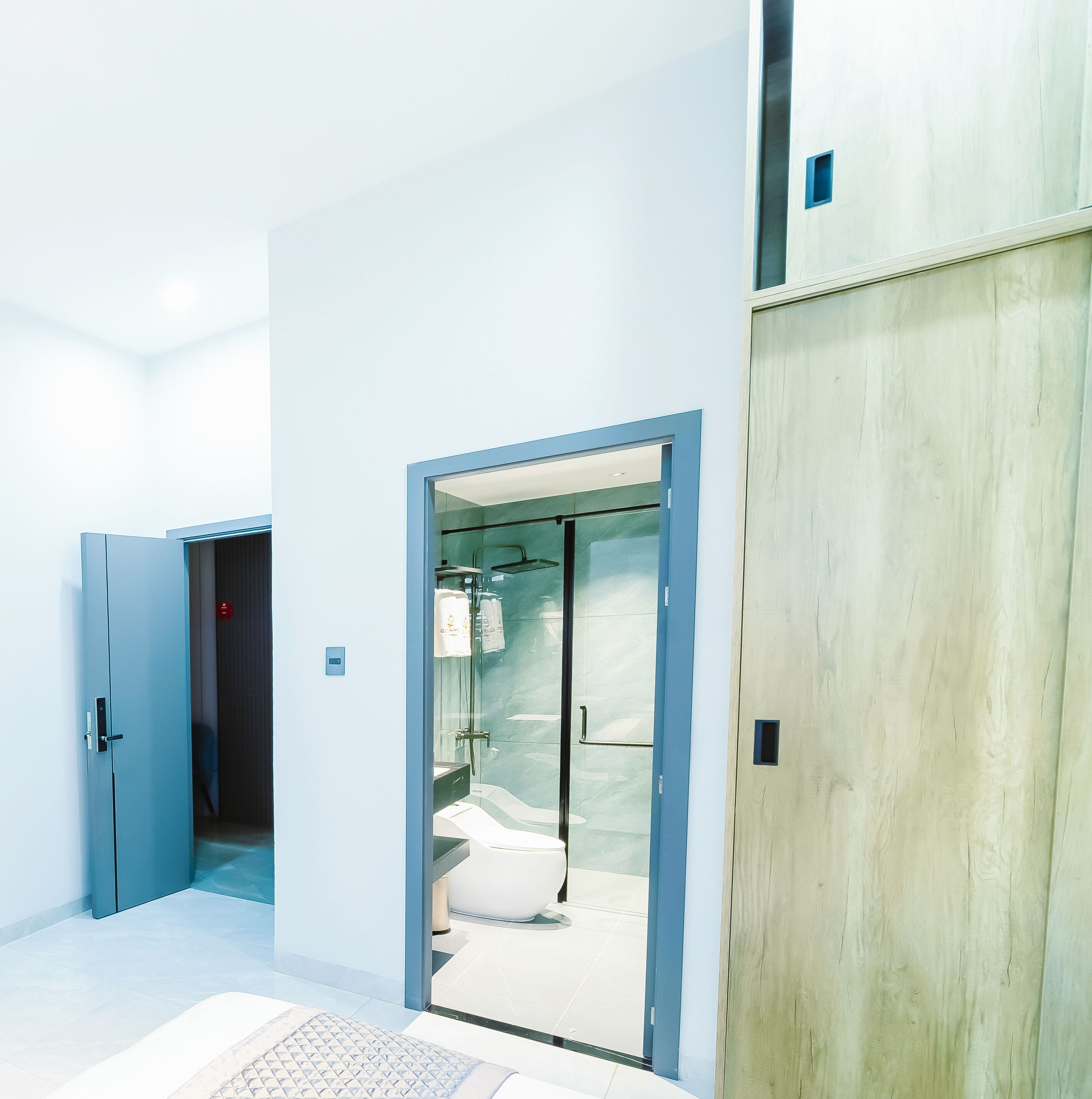 Moderni hotellihuone, jossa on suuri peili, puinen vaatekaappi ja lasinen suihkuseinä.