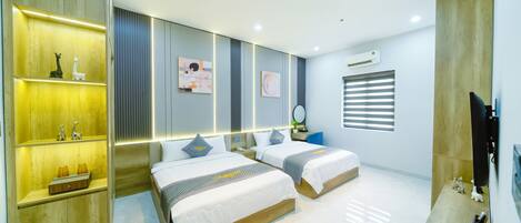 A modern hotel room with two beds, a wooden wardrobe, a vanity with a mirror, and a window with blinds.