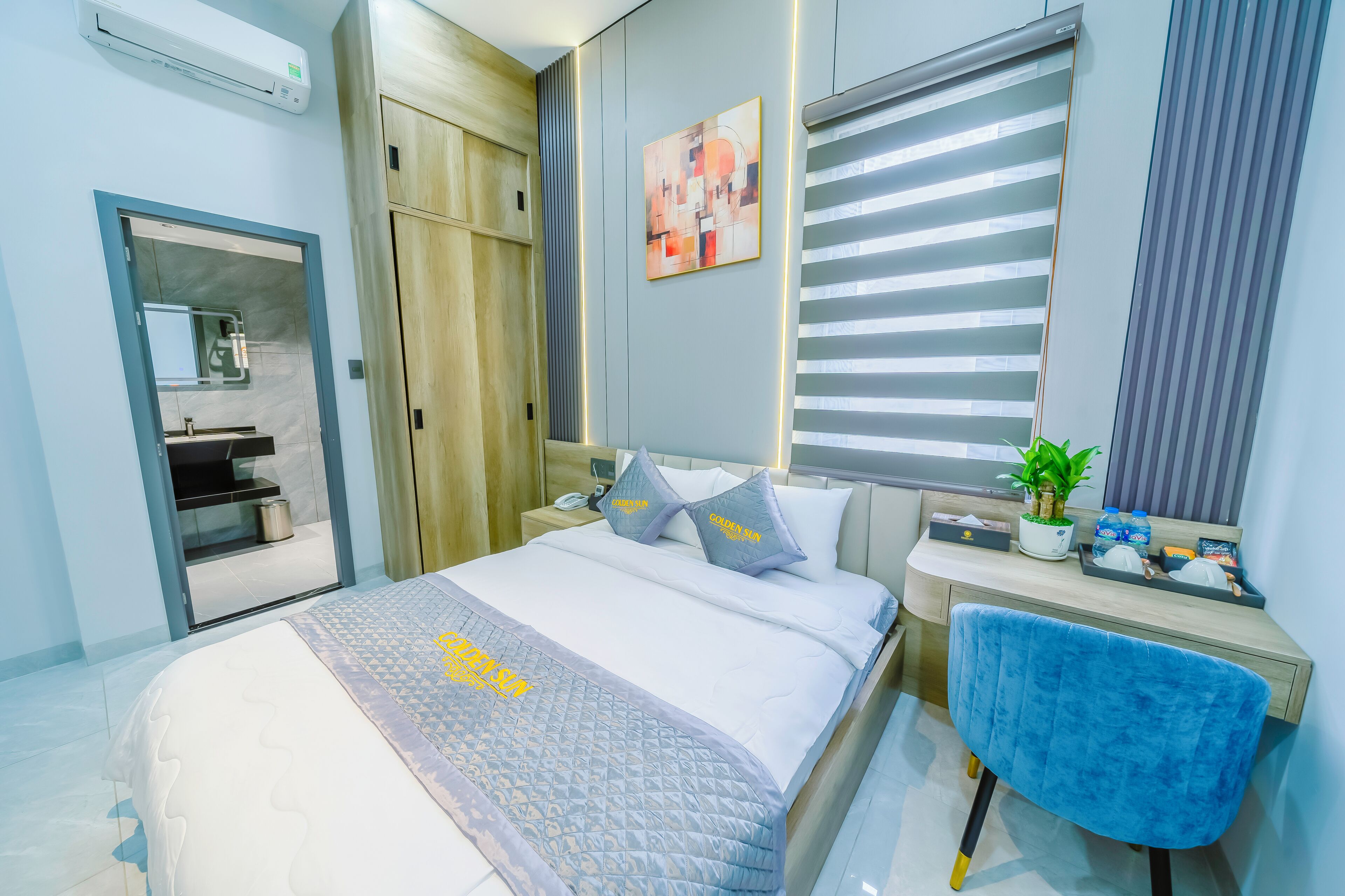 Ein modernes Hotelzimmer mit Bett, Nachttisch, Schreibtisch, Stuhl und einem Fenster mit Jalousien.