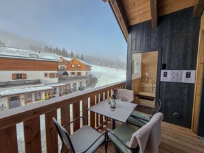 A wooden deck with a table and chairs, overlooking a snowy landscape and a ski lift.